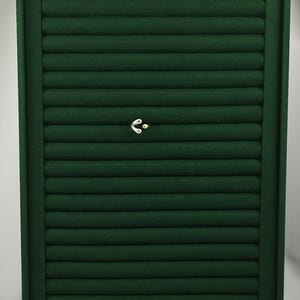 May include: A rectangular dark green velvet jewelry display tray featuring multiple horizontal padded slots for organizing rings. A small silver-toned ring with a minimalist curved design and a single embedded stone is positioned in the center.