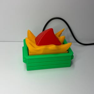 May include: A green rectangular container filled with yellow, triangular shapes, and a red triangular shape. The container is sitting on a white surface. The image is well-lit and the colors are vibrant.
