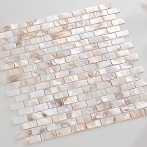 May include: A mosaic tile sheet featuring small, rectangular tiles arranged in a brick pattern. The tiles have a pearlescent finish with white, cream, and tan tones. Ideal for interior design projects, the tiles measure approximately 2.5 cm x 1.25 cm.