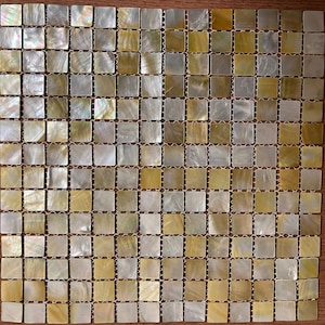 Op de afbeelding: Een vierkante mozaïektegelplaat bestaande uit talrijke kleine, vierkante tegels. De tegels hebben een parelmoerachtige, iriserende kwaliteit met tinten goud, crème en zilver. De tegels zijn gerangschikt in een rasterpatroon, geschikt voor interieurontwerp.