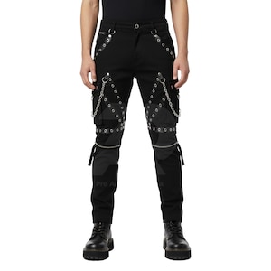 Może przedstawiać: Czarne spodnie ze srebrnymi oczkami, łańcuchami i paskami. Projekt charakteryzuje się różnorodnymi fakturami i detalami, w tym zamkami błyskawicznymi na kolanach. Spodnie są zestawione z czarnymi butami, tworząc odważny, odważny wygląd.