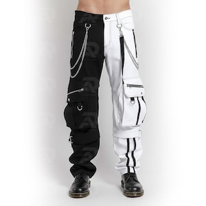 Op de afbeelding: Zwart-witte broek met meerdere zakken, ritsen en zilveren kettingaccenten. De broek heeft een uniek ontwerp met een zwart linkerbeen en een wit rechterbeen, met een moderne, edgy stijl.