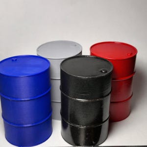 May include: A collection of miniature barrels in blue, gray, black, and red. The barrels are cylindrical with a rounded top and bottom. A ruler is placed in front of the barrels, with the first barrel measuring approximately 1 inch in diameter.