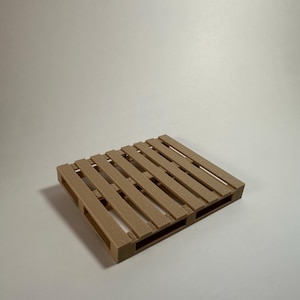 Puede incluir: Una pequeña paleta de madera de color marrón claro. Tiene forma rectangular con múltiples listones horizontales y soportes verticales, creando un patrón de rejilla. El diseño es simple y funcional, adecuado para exhibiciones en miniatura o manualidades.