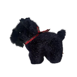 Puede incluir: Un perro de peluche negro de raza Scottish Terrier con una cinta a cuadros roja y verde alrededor del cuello. El perro tiene una apariencia esponjosa y texturizada y está sobre un fondo blanco. El perro de juguete es un artículo decorativo.