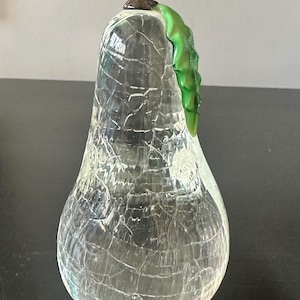 Puede incluir: Objeto decorativo en forma de pera de vidrio transparente con efecto craquelado. La pera tiene un tallo marrón y un detalle de hoja verde. Probablemente sea un artículo decorativo para el hogar o la oficina.