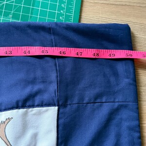 Peut inclure: Un tissu bleu marine avec un motif blanc et beige est mesur&eacute; avec un m&egrave;tre ruban rose. Le tissu mesure environ 127 cm de large. Un tapis de coupe vert et une surface en bois sont en arri&egrave;re-plan.
