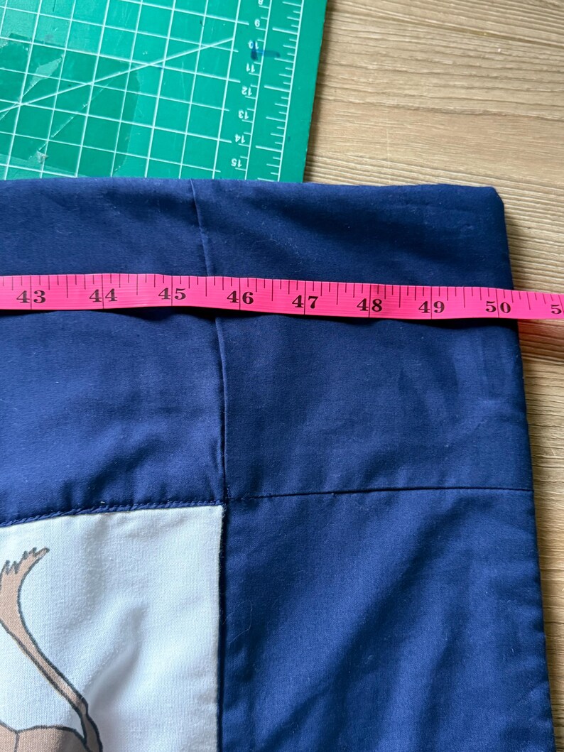 Peut inclure: Un tissu bleu marine avec un motif blanc et beige est mesur&eacute; avec un m&egrave;tre ruban rose. Le tissu mesure environ 127 cm de large. Un tapis de coupe vert et une surface en bois sont en arri&egrave;re-plan.