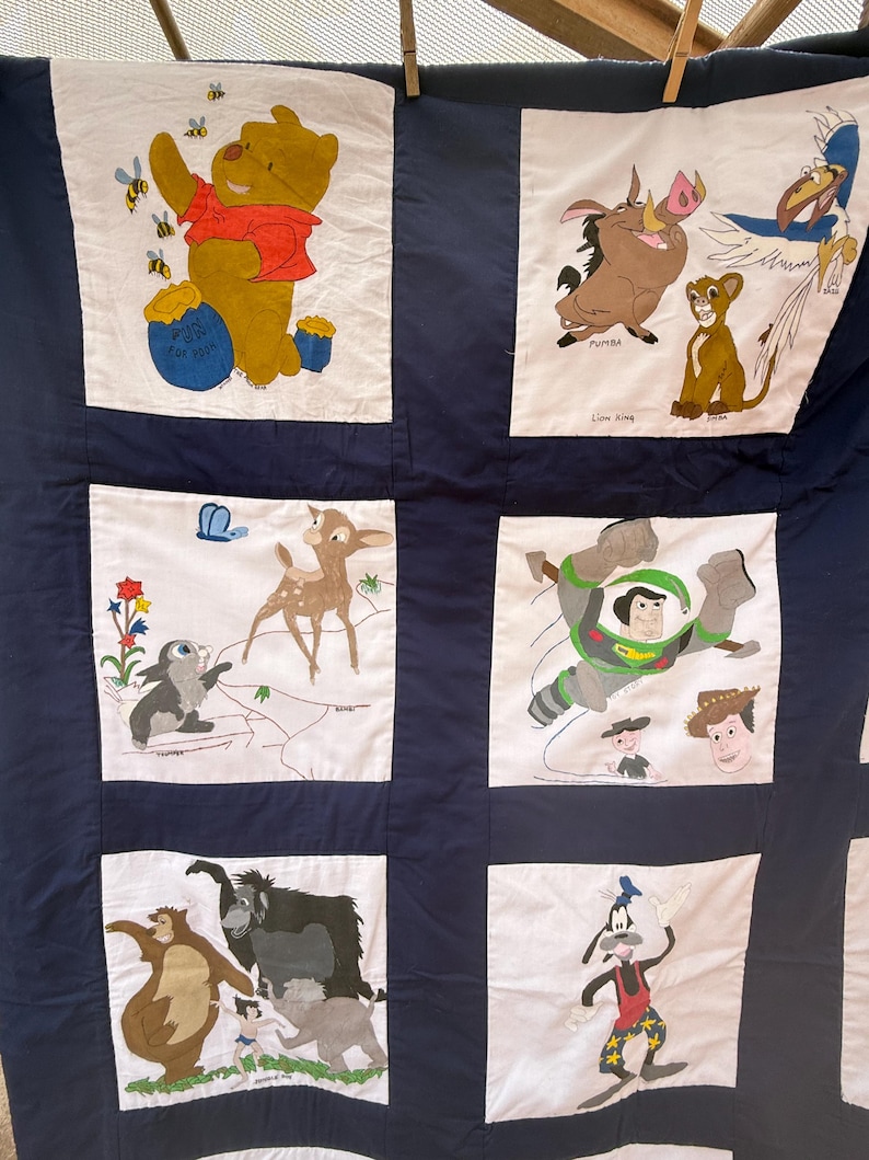 Peut inclure: Une courtepointe faite &agrave; la main avec des personnages Disney. La courtepointe pr&eacute;sente des panneaux avec Winnie l'ourson, Simba, Timon, Pumbaa, Bambi, Buzz l'&Eacute;clair, Baloo et Dingo. Les personnages sont sur fond blanc avec une bordure bleu marine.