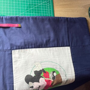 Peut inclure: Une taie d'oreiller bleu marine avec un carr&eacute; blanc repr&eacute;sentant un dessin de Mickey Mouse. Le dessin montre Mickey Mouse avec une chemise rouge et des gants blancs. Un ruban &agrave; mesurer rose indique 152 cm.