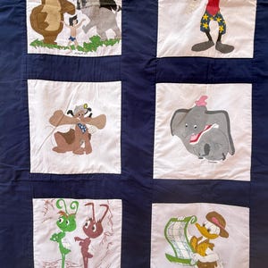 Peut inclure: Une courtepointe patchwork avec divers personnages de dessins anim&eacute;s Disney. La courtepointe a un fond bleu fonc&eacute; avec des carr&eacute;s blancs, chacun affichant un personnage diff&eacute;rent, dont Baloo, Mowgli et Dumbo. Les personnages sont de couleurs vari&eacute;es, dont le marron, le gris et le vert.