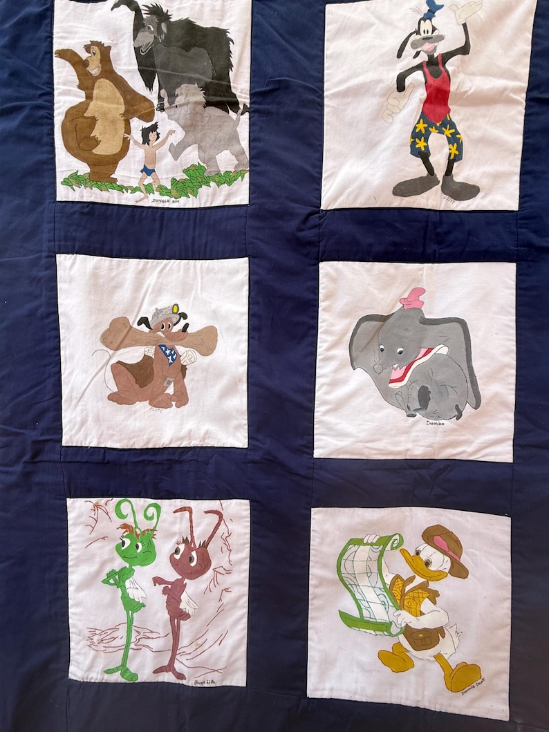 Peut inclure: Une courtepointe patchwork avec divers personnages de dessins anim&eacute;s Disney. La courtepointe a un fond bleu fonc&eacute; avec des carr&eacute;s blancs, chacun affichant un personnage diff&eacute;rent, dont Baloo, Mowgli et Dumbo. Les personnages sont de couleurs vari&eacute;es, dont le marron, le gris et le vert.