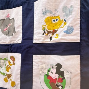Peut inclure: Une courtepointe faite &agrave; la main avec des personnages de dessins anim&eacute;s tels que Dumbo, Bob l'&eacute;ponge et Mickey Mouse. La courtepointe a un fond bleu marine avec des carr&eacute;s blancs pr&eacute;sentant les personnages. Les personnages sont de couleurs vari&eacute;es, dont le jaune, le gris et le rouge.