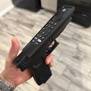 May include: A black plastic remote control housing shaped like a handgun. The remote features a circular navigation pad, playback buttons, and dedicated streaming service buttons for Netflix, Peacock, and Prime Video, with a blue power button.