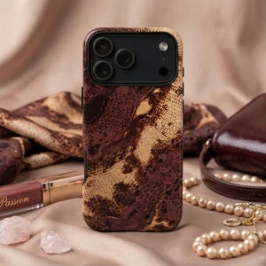 May include: A mobile phone case with a brown and beige snakeskin design. Beside it are a brown handbag, a pearl necklace, and a lipstick tube with the text "La Passion".