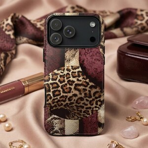 Op de afbeelding: Een telefoonhoesje met patroon met een luipaardprint, bordeauxrode en bruine accenten. De hoes ligt naast een tube lippenstift, een bordeauxrode handtas en een parelketting. De achtergrond is een satijnen stof.