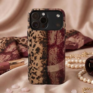 Op de afbeelding: Een smartphonehoesje met een gemengd patroon van luipaardprint en een bordeauxrood slangenleerontwerp. De hoes wordt omringd door accessoires, waaronder een lippenstift, een sjaal en een parelketting.
