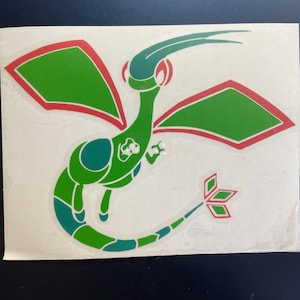 Może przedstawiać: Zielono-turkusowa grafika stylizowanej istoty z czerwonymi akcentami na białym tle. Stworzenie ma duże skrzydła, długi ogon i charakterystyczny kształt głowy. Projekt przypomina postać z kreskówki lub gry wideo.