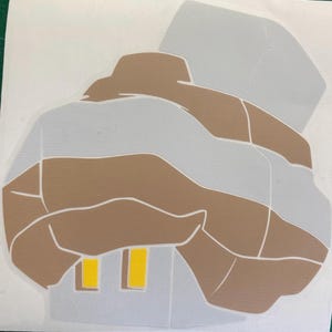 May include: A sticker featuring a stylized illustration of a house. The design uses shades of gray and brown, with yellow rectangles representing windows. The house shape is outlined in white.