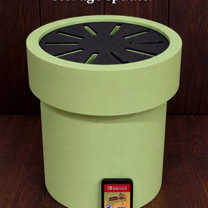 May include: A light green Switch game storage spinner with a black top featuring cut-out slots. The text "Switch Game Storage Spinner" is at the top. A Nintendo Switch game cartridge is next to the spinner.