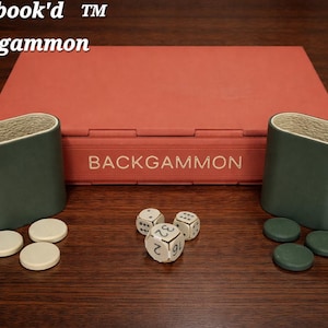 May include: A backgammon set with a red case and the word "BACKGAMMON" printed on it. Two green dice cups, white and green game pieces, and three dice are arranged on a wooden surface. The text "Playbook'd Backgammon" is in the upper left corner.