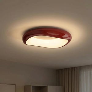 May include: A contemporary ceiling light in a deep red hue, featuring a distinctive, flowing form. The light has a polished surface and emits a bright, white glow. The design is minimalist and modern, suitable for diverse interior settings.