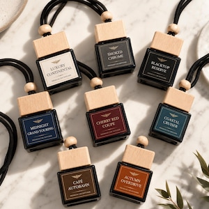 May include: Eight square glass car diffusers with light wood caps and black hanging cords. Each bottle features a label with a unique name such as Luxury Continental, Smoked Chrome, Blacktop Reserve, Midnight Grand Touring, Cherry Red Coupe, Coastal Cruiser, Café Autobahn, and Autumn Overdrive.
