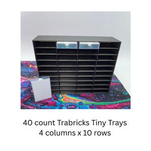 Può includere: Un organizer nero con 40 scomparti disposti in 4 colonne e 10 righe, etichettato 40 count Trabricks Tiny Trays 4 columns x 10 rows. L'unità presenta due piccoli contenitori in plastica trasparente inseriti nella parte superiore e uno separato.