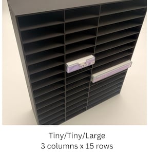 May include: A dark grey storage organiser featuring a grid of 3 columns and 15 rows of rectangular compartments. Two clear plastic drawers with white handles are inserted into the slots. The text Tiny/Tiny/Large 3 columns x 15 rows is visible.