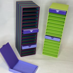 May include: Three colorful desk organizers. One is a tall, striped rainbow design with purple drawers. Another is lime green with purple drawers. A purple box with a lid is open in the foreground. These organizers are ideal for office or craft supplies.
