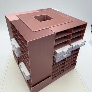 May include: A rose gold desktop organiser featuring a square rotating base with multiple open storage shelves and several small, clear plastic drawers with white handles. The top surface has a square cutout in the centre for additional storage.