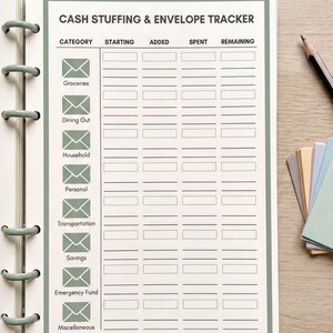 a cash stuffing and envelope tracker notebook on a wooden surface, with a pen and some colored paper nearby.
