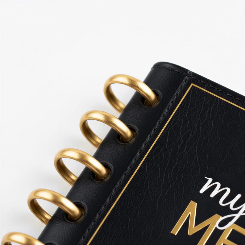 a close-up view of a black spiral-bound notebook with gold rings, resting on a white background.