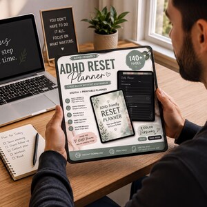 A person is sitting at a desk, holding a tablet or e-reader displaying an ADHD-friendly reset planner. The desk has a laptop, a notebook, and a potted plant.
