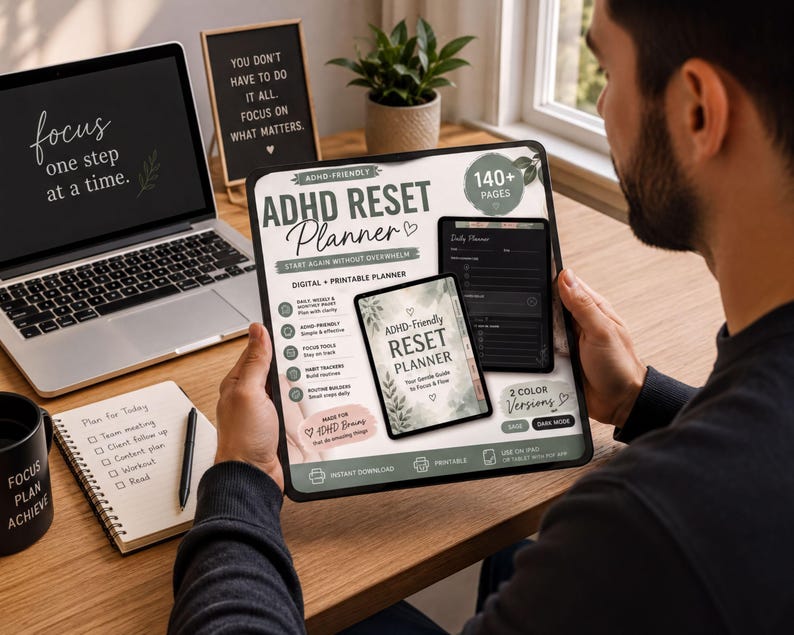 A person is sitting at a desk, holding a tablet or e-reader displaying an ADHD-friendly reset planner. The desk has a laptop, a notebook, and a potted plant.