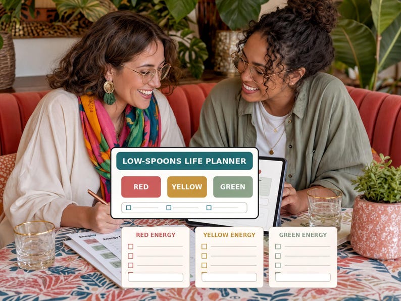 Two women are sitting at a table, smiling and looking at a laptop screen displaying a "Low-Spoons Life Planner" with color-coded sections for "RED", "YELLOW", and "GREEN ENERGY".