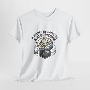 Peut inclure: T-shirt blanc avec un motif d'un cerveau souriant portant des lunettes, entouré d'éléments de circuits imprimés. Le texte indique "Powered by Caffeine & Algorithms". Le motif comprend un code binaire et une manette de jeu.