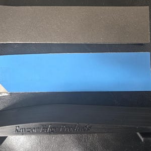 May include: An assortment of sharpening tools. The image shows a black plastic guide with the text "Razor Edge Products", a blue rectangular piece, and a gray rectangular piece. The items are arranged on a dark surface.