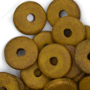 May include: A pile of round, wooden beads in a muted mustard yellow color. The beads have a hole in the center and are stacked on top of each other.