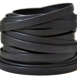 May include: A coiled length of flat, matte black leather cord. The cord is wrapped in multiple overlapping layers, creating a cylindrical shape with a smooth, consistent texture and uniform width throughout the entire length of the material.