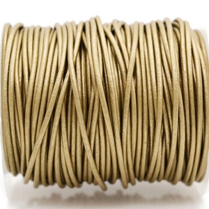 May include: A spool of metallic gold round cord wrapped in a continuous coil. The cord has a smooth, uniform texture and a consistent thickness throughout the entire length, wound tightly around a cylindrical core to maintain its shape.