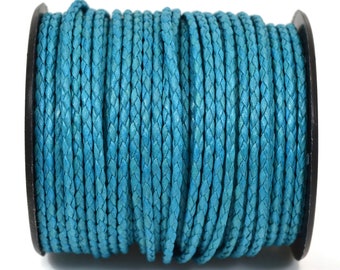 Puede incluir: Un carrete de cordón trenzado de color turquesa brillante enrollado cuidadosamente alrededor de una bobina de plástico negro. El cordón presenta una textura tejida consistente en toda su longitud, creando un aspecto uniforme al enrollarse.