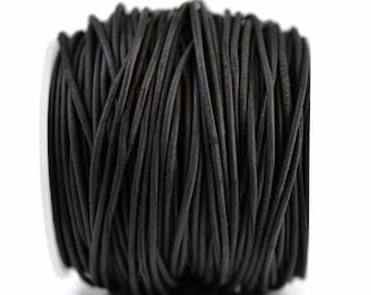 May include: A spool of black leather cord wrapped in a continuous coil. The cord has a smooth, matte texture and a consistent round profile, wound tightly around a central white cylindrical core, creating a dense, uniform black appearance.