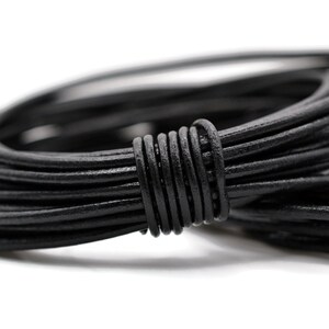 May include: A close-up shot of a bundle of black leather cord. The cord is tightly coiled, with several loops visible. The leather appears to be smooth and has a slight sheen. The background is plain white.