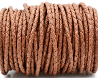 Puede incluir: Un carrete de cordón trenzado de color marrón claro con una textura tejida consistente. El cordón está enrollado firmemente en múltiples capas paralelas, creando una forma cilíndrica con una apariencia uniforme y un acabado mate en toda su longitud.