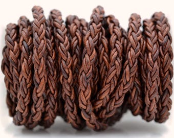 May include: A continuous length of dark brown leather cord featuring a braided construction. The cord is coiled into multiple overlapping loops, showcasing a textured, matte finish with natural variations in the deep brown color throughout.