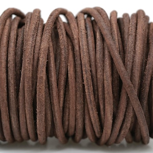 May include: A spool of dark brown leather cord. The cord is tightly wound, revealing a textured, slightly rough surface. The color is a rich, earthy brown, suitable for jewelry making or crafting projects.