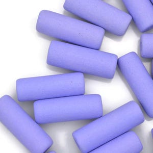 May include: A group of lavender colored ceramic cylinder beads. The beads are smooth and have a slightly textured surface.
