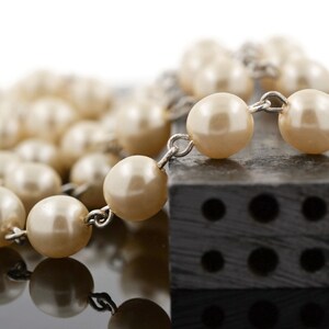 May include: A strand of white faux pearl beads with silver metal connectors, resting on a black rectangular block with six holes.
