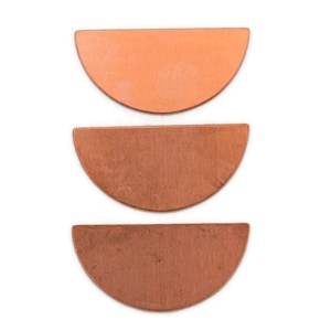 May include: Three copper-colored, semi-circular metal pieces arranged vertically against a white background. The pieces vary slightly in shade, ranging from light orange to a darker, more reddish-brown.